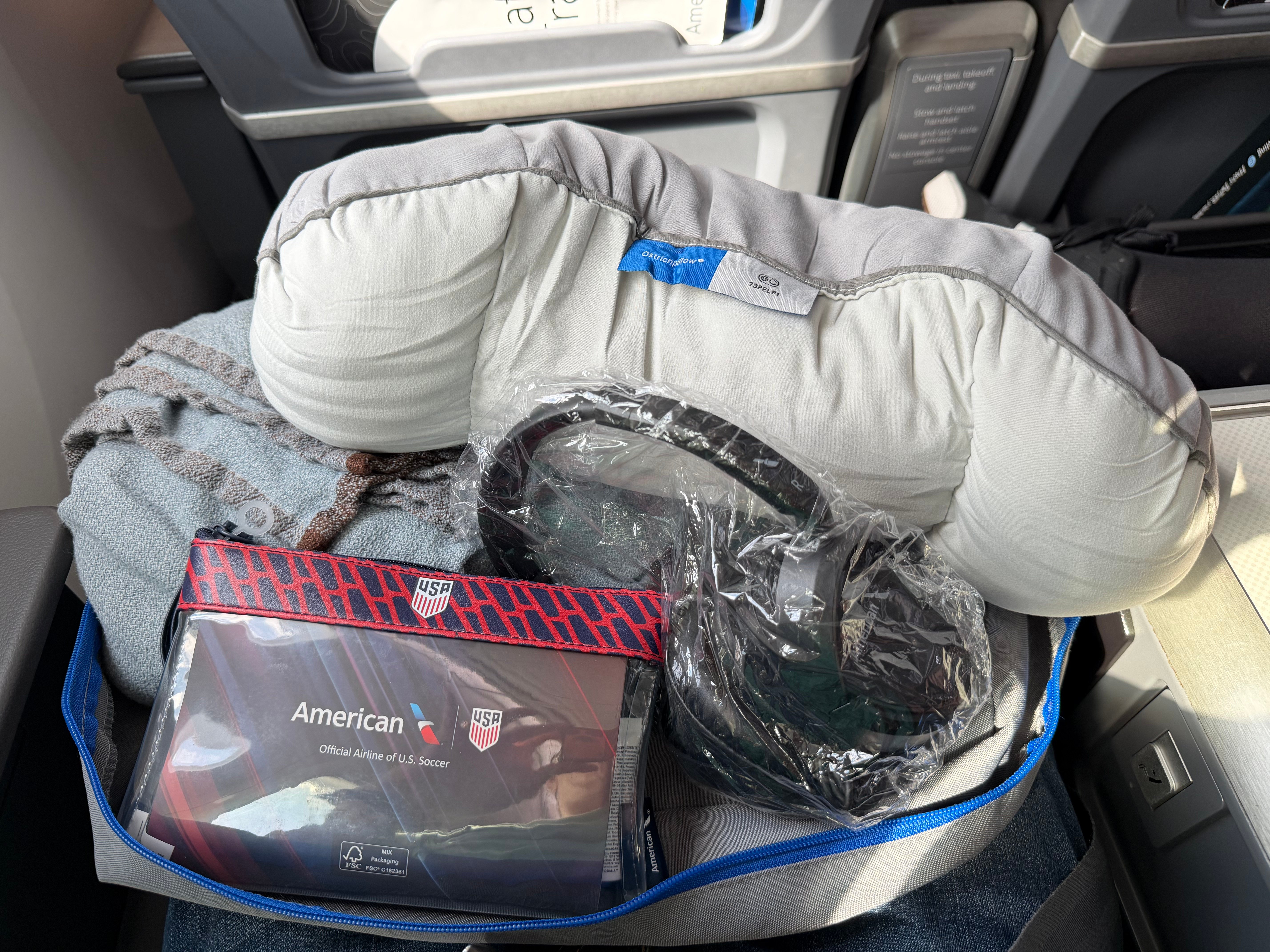 Open Main Cabin Extra welcome bag with bedding, headphones, and an amenity kit.