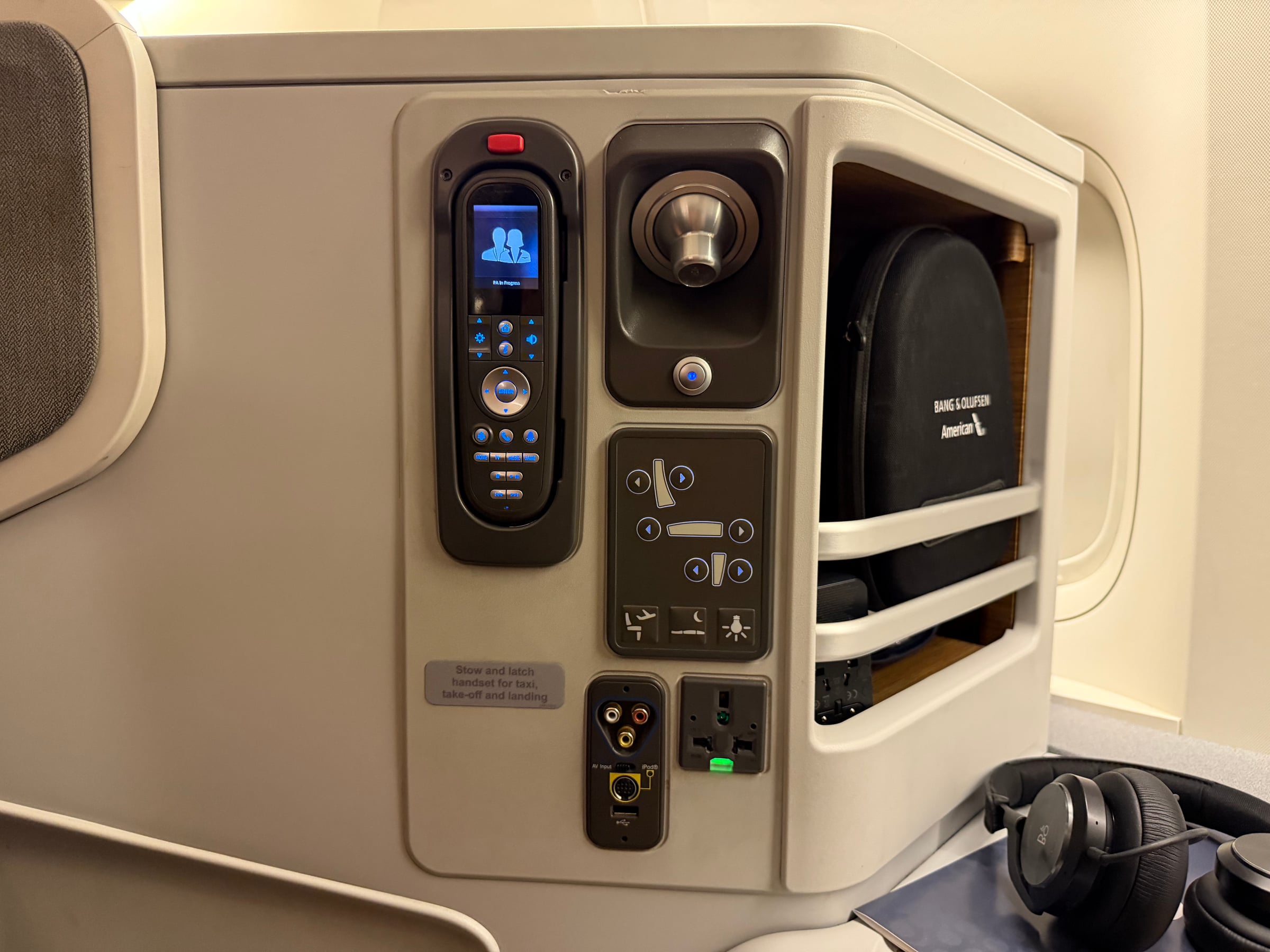 Seat controls, handheld IFE remote, power outlets, and storage at the American 777 Business Class seat.