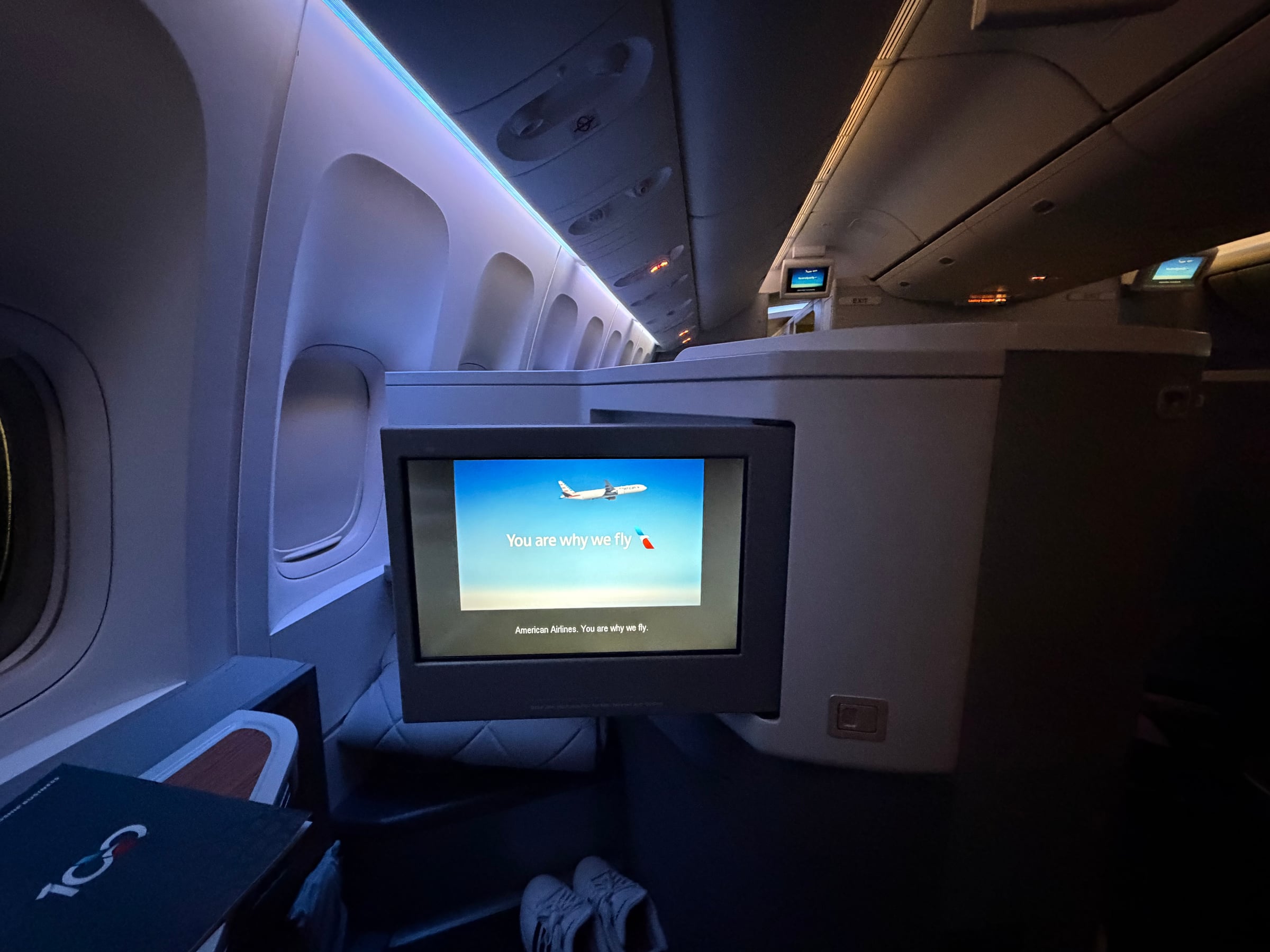 American Airlines Business Class seat and IFE screen under blue cabin lighting.