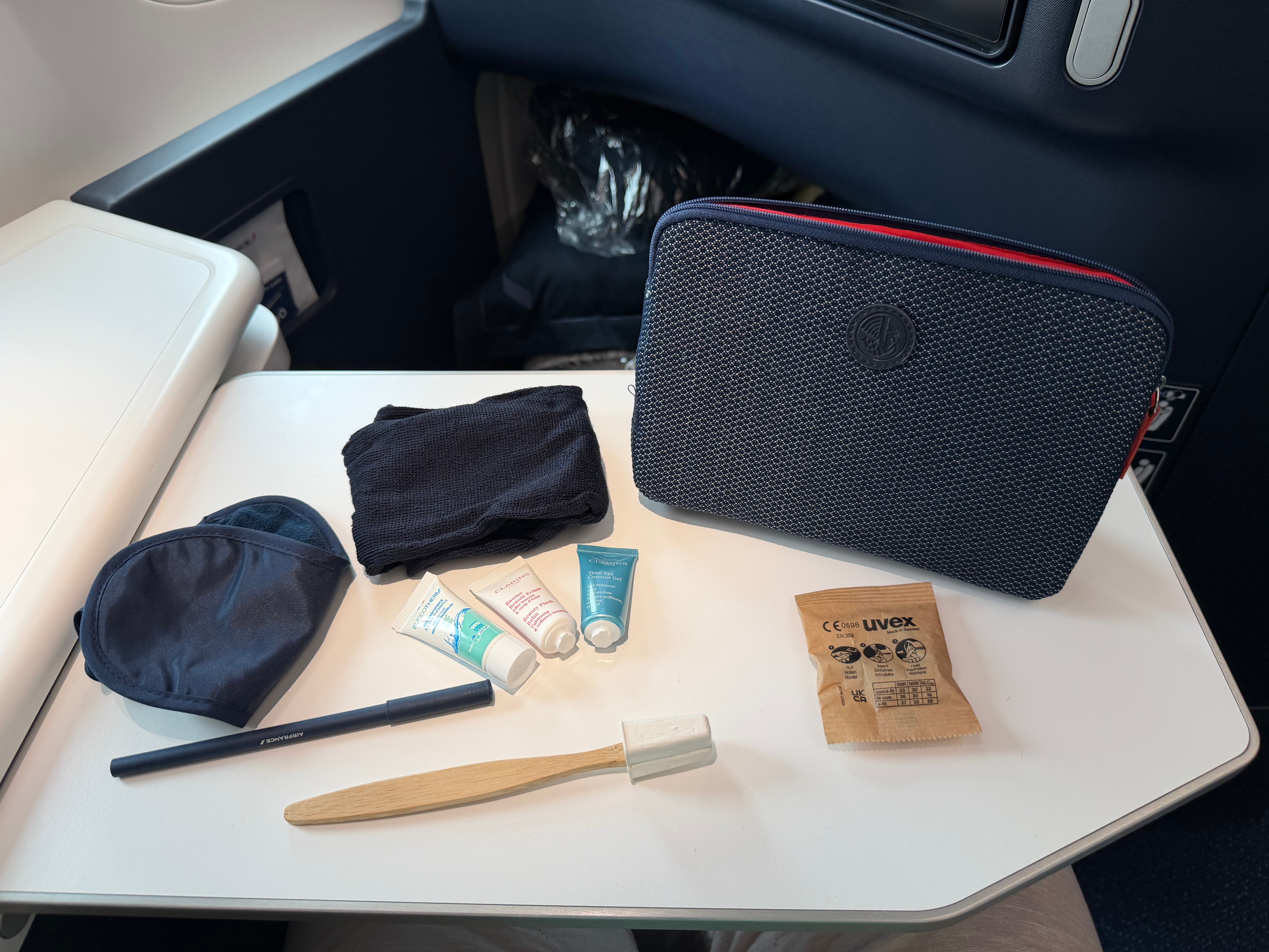 Amenity kit contents with Clarins face balm and eye gel, socks, eye mask, and dental items.