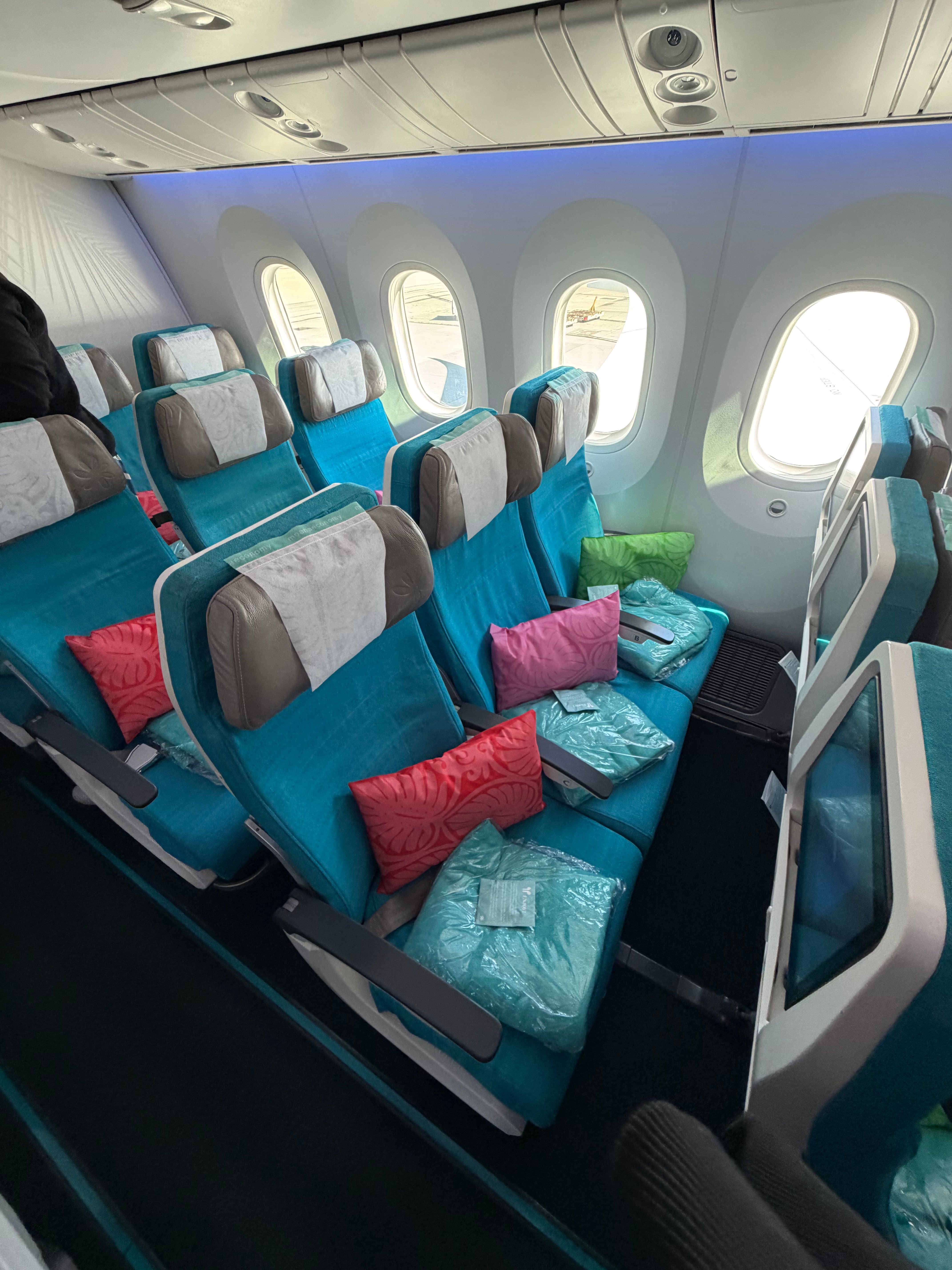 Air Tahiti Nui Moana Economy cabin with turquoise seats and colorful pillows.
