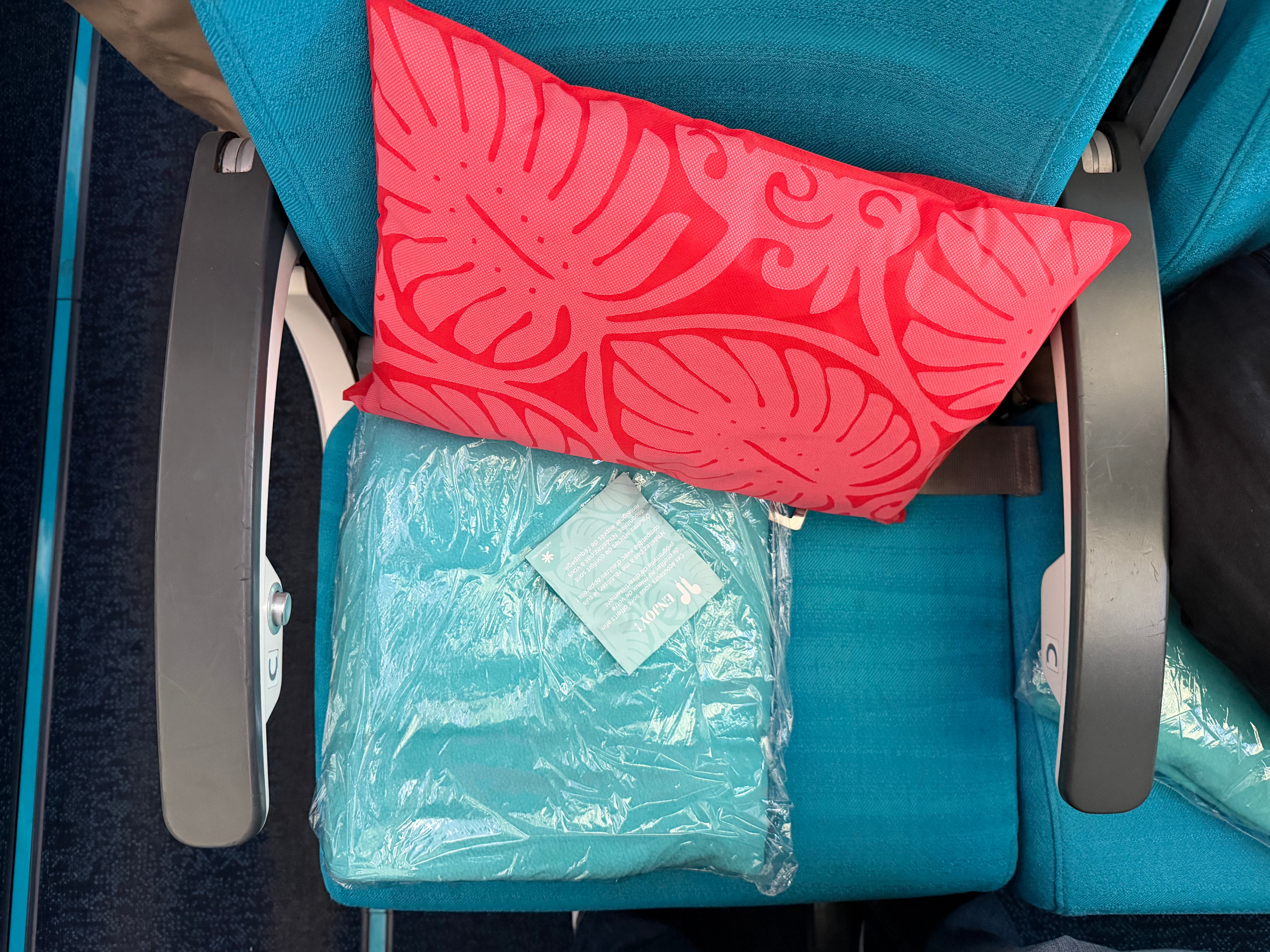 Colorful pillow and packaged blanket placed on an Air Tahiti Nui Economy seat.