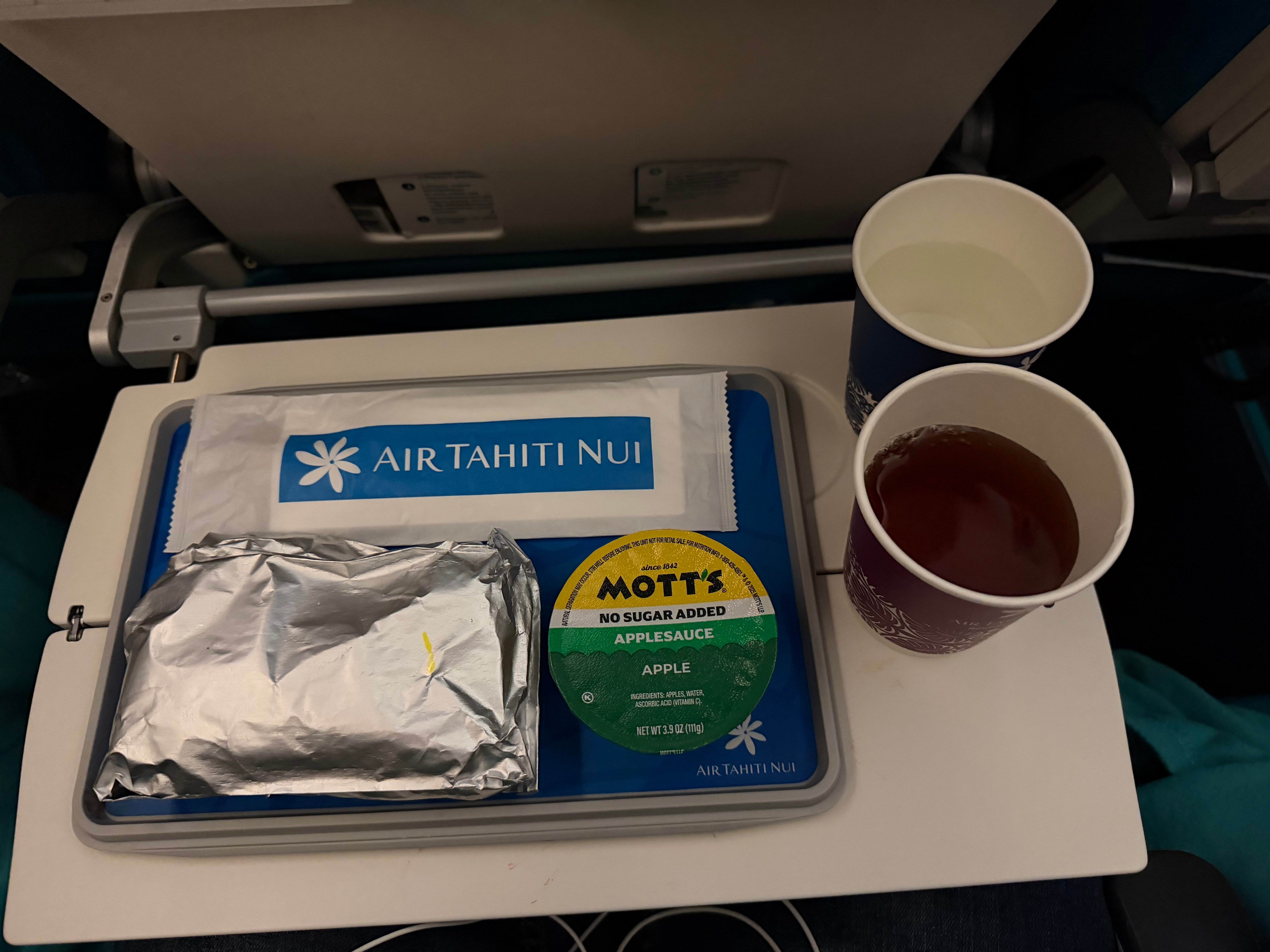Covered Air Tahiti Nui prearrival meal with a drink and applesauce.