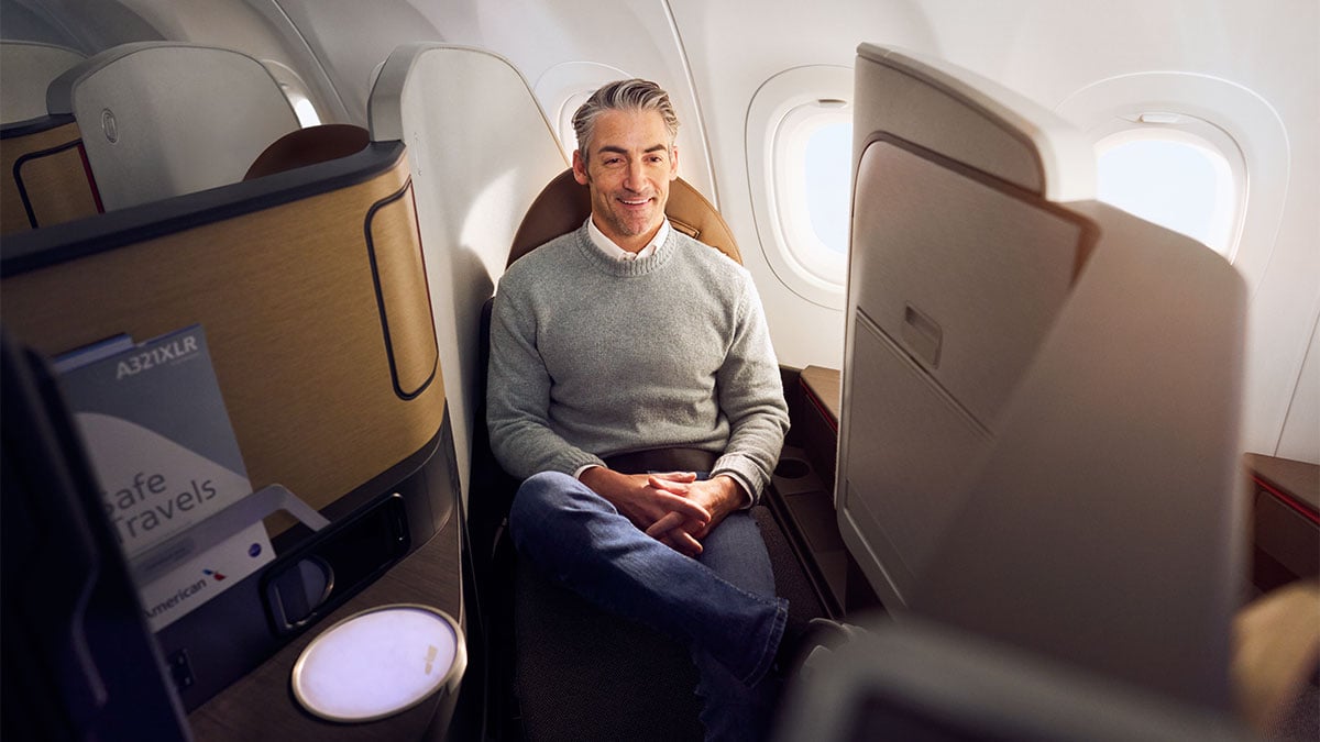 Passenger seated in an American Airlines A321XLR Flagship Suite beside the window, with a privacy partition and personal screen.