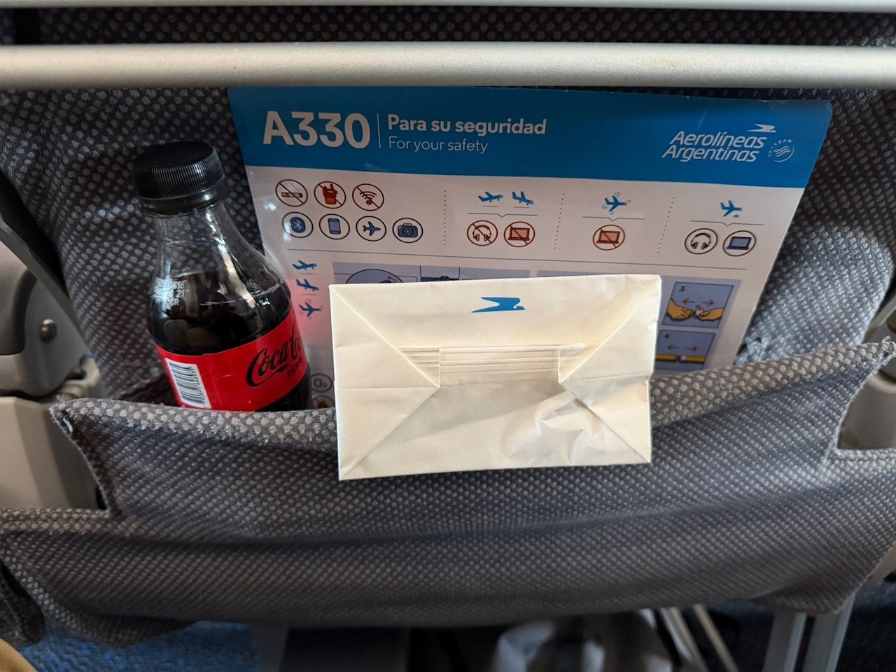 Seat pocket with safety card, Coca Cola Zero bottle, and snack on Aerolíneas Argentinas.