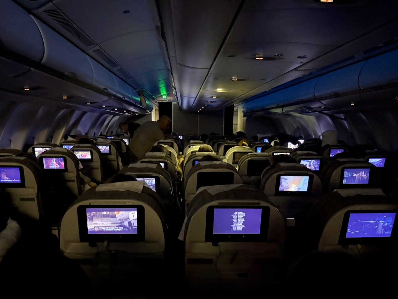 Darkened Aerolíneas Argentinas A330 economy cabin with IFE screens during the overnight portion of the flight.