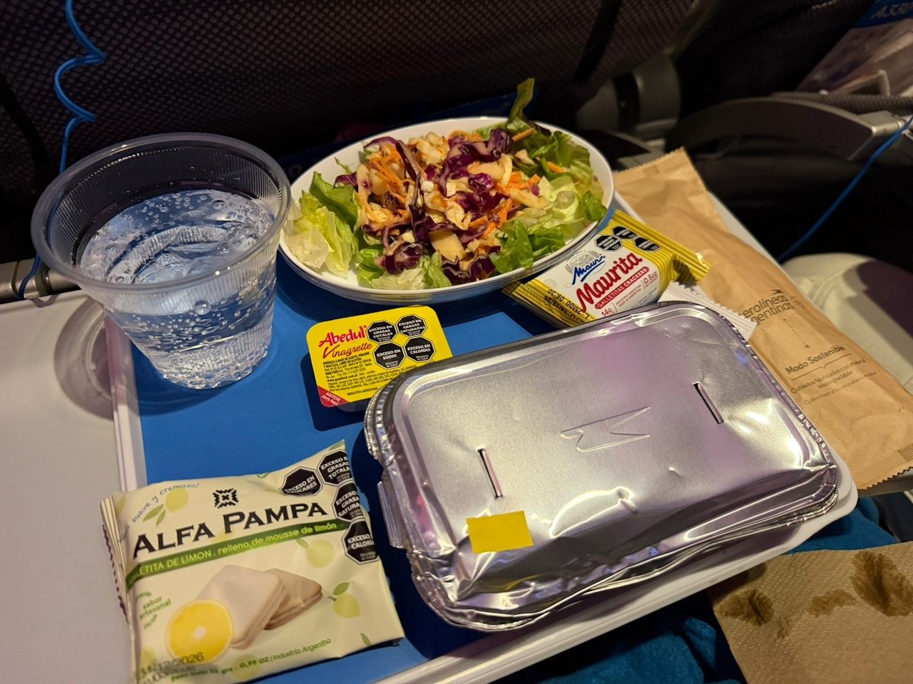Aerolíneas Argentinas dinner tray with water and foil-covered main course.