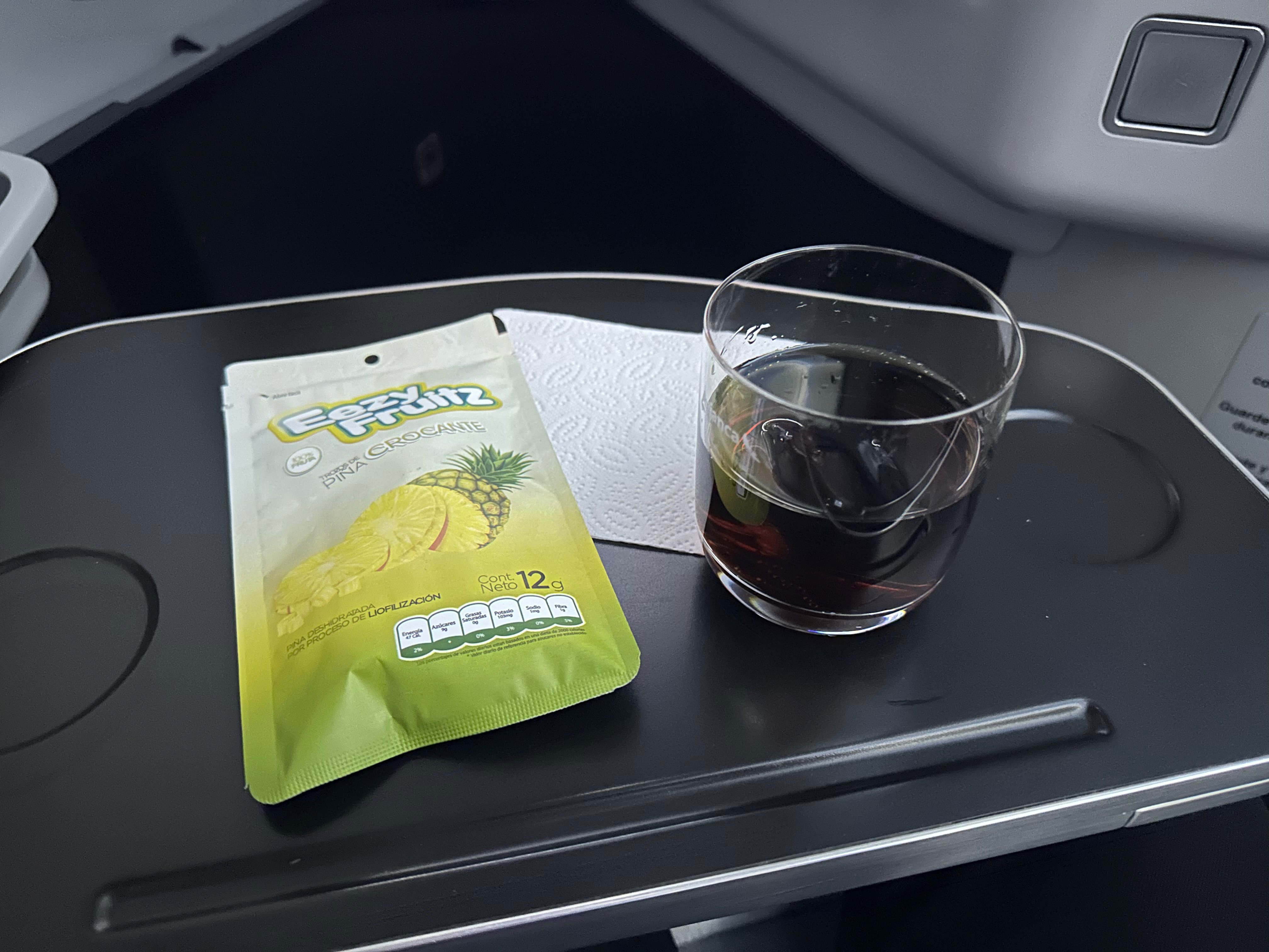 Packaged pineapple snack and a drink on the tray table.
