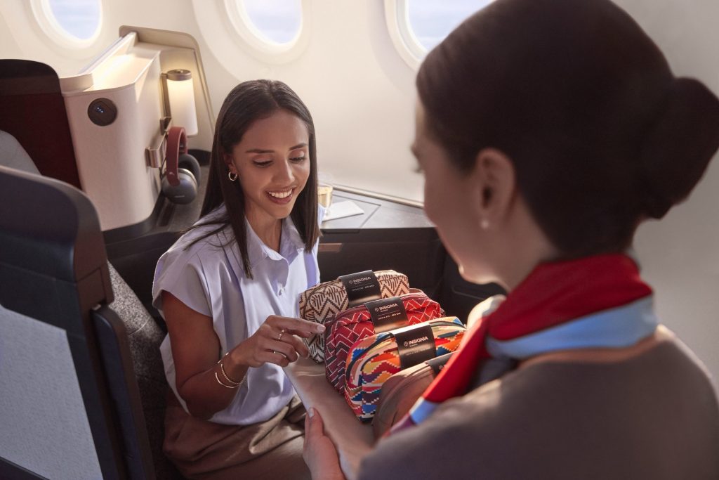 Avianca cabin crew member offering a selection of patterned INSIGNIA amenity kits.