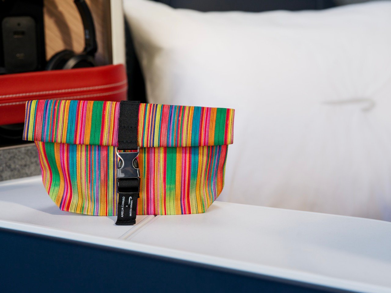 Colourful striped Club World amenity kit displayed beside a pillow.