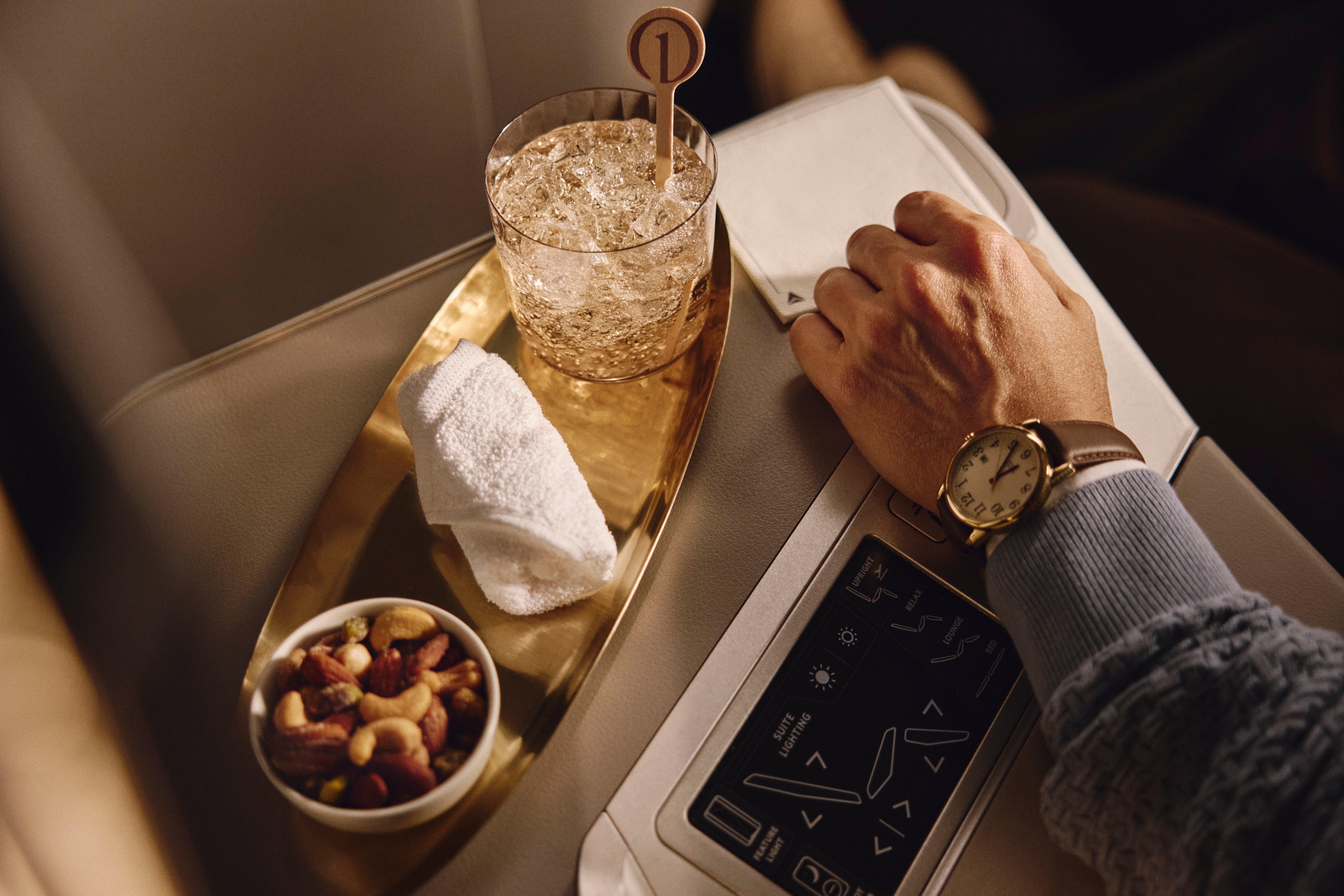 Drink, rolled towel, and bowl of nuts arranged on a tray beside a Delta One passenger.