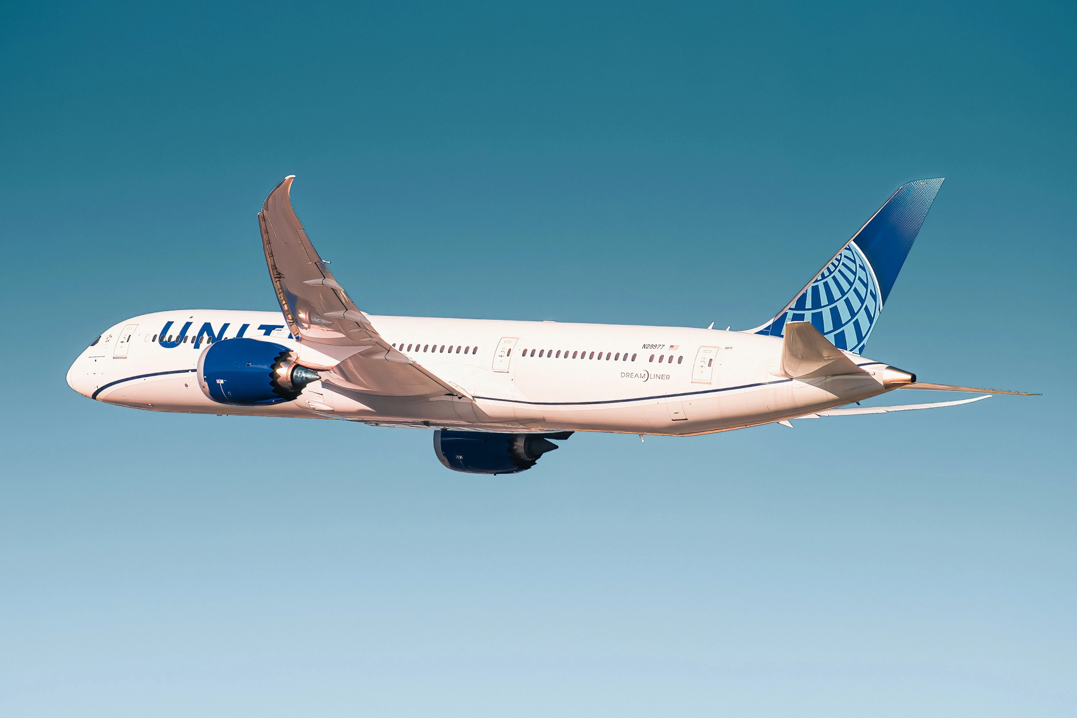 A United Airlines Boeing 787 Dreamliner flying against a clear blue sky.
